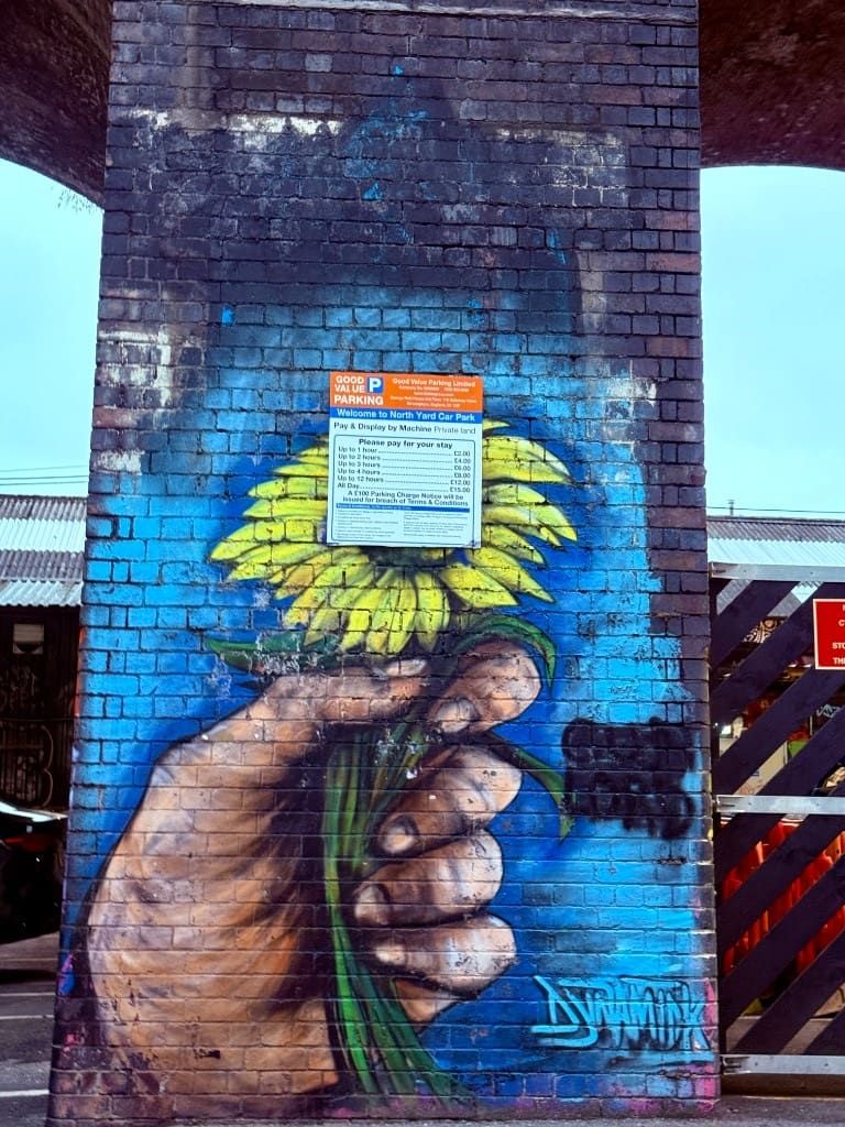 Street-art mural of a hand holding a sunflower painted on a brick pillar in Digbeth